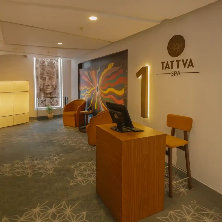 Reception area of Tattva Wellness Spa at Four Points by Sheraton, Sholinganallur, Chennai, featuring a modern wooden desk, cozy mustard chairs, and a colorful mural that adds warmth to the serene spa ambiance.