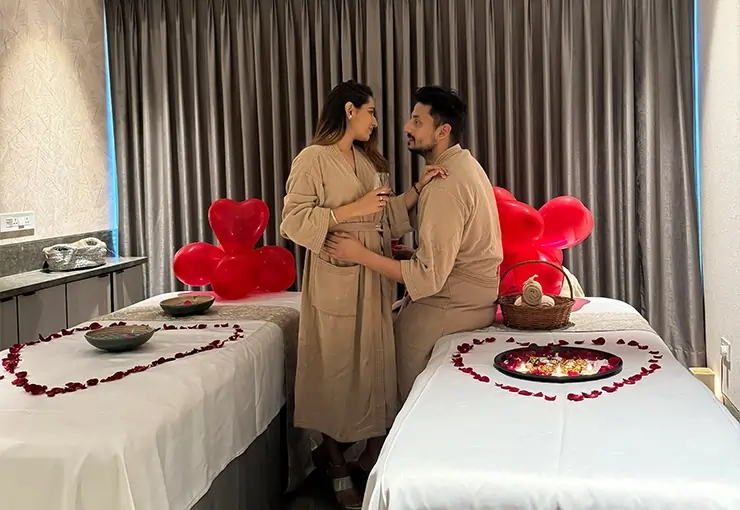 A romantic couple spa room setup with two decorated spa beds adorned with rose petals and flower bowls, a couple in spa robes enjoying a cozy moment, surrounded by heart-shaped balloons creating a perfect couple spa experience at tattva spa