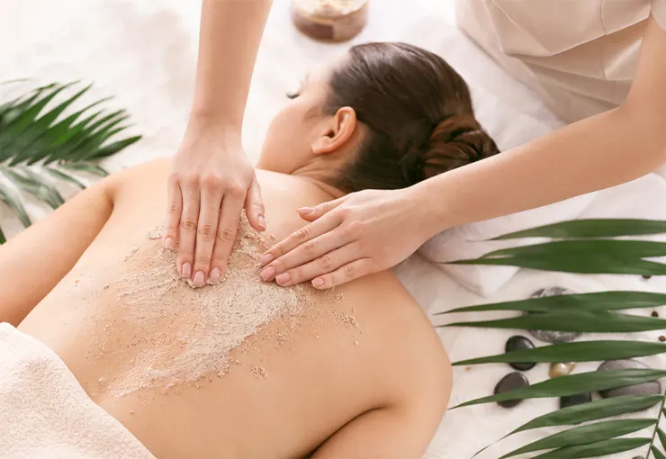 A woman receives a relaxing back scrub treatment at a spa, surrounded by natural leaves and healing elements—a thoughtful and pampering Rakhi gift for your sibling to unwind and rejuvenate.