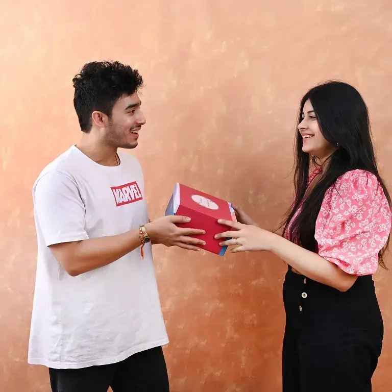 A happy brother and sister exchanging a beautifully wrapped pink gift box, smiling warmly at each other – a perfect moment of Last-Minute Rakhi Gifting that captures love, joy, and sibling bonding.