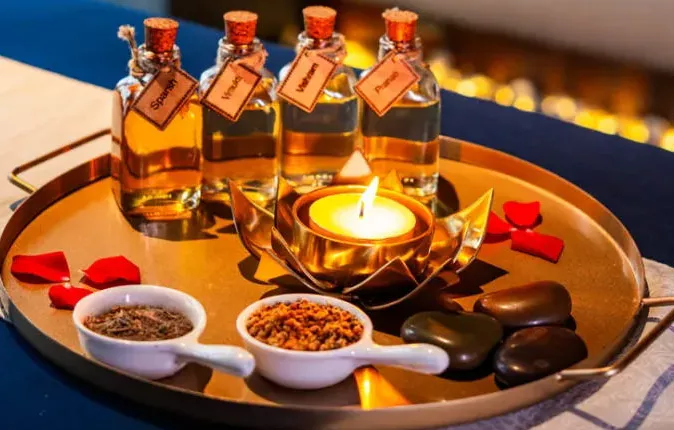 Various type of massage oils placed on metal plate with black stones, flower petals and diya 