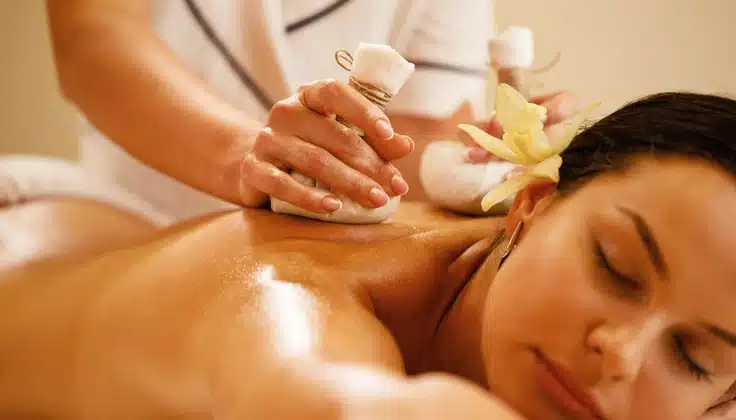 Woman receiving a warm herbal compress massage for relaxation at a spa.
