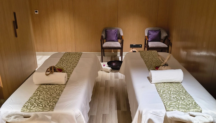 Couple spa treatment room with two massage beds and seating at a hotel spa.