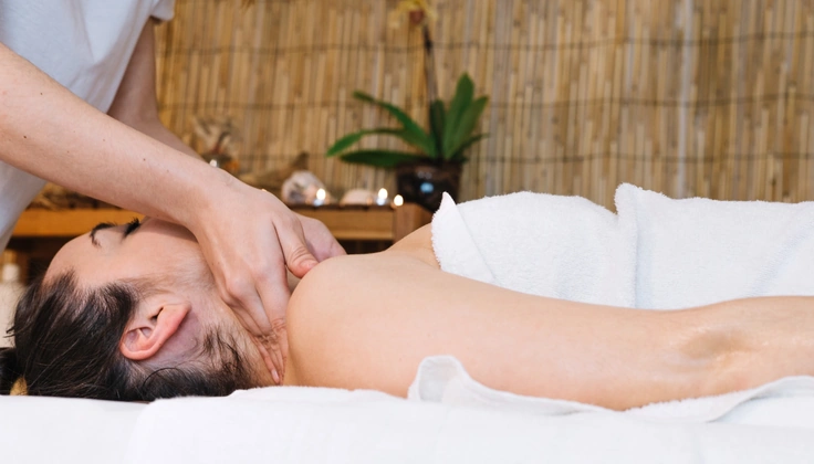 herapist applying deep pressure to the neck and upper shoulder muscles during a massage.